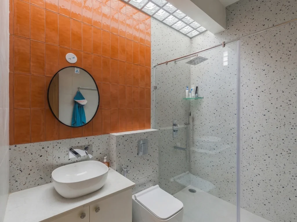 Contemporary bathroom design with vibrant orange vertical tiles, terrazzo-patterned walls, a floating vanity, and a frameless glass shower partition.