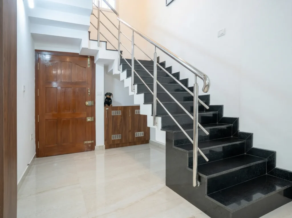 Internal residential staircase featuring polished black granite steps, stainless steel railings, and a solid wood main door.