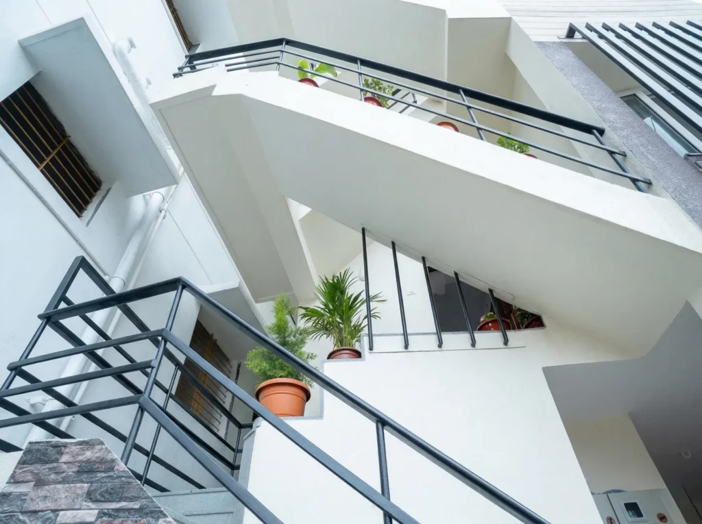 Modern external zig-zag staircase design with black safety railings and decorative potted plants for an urban villa.