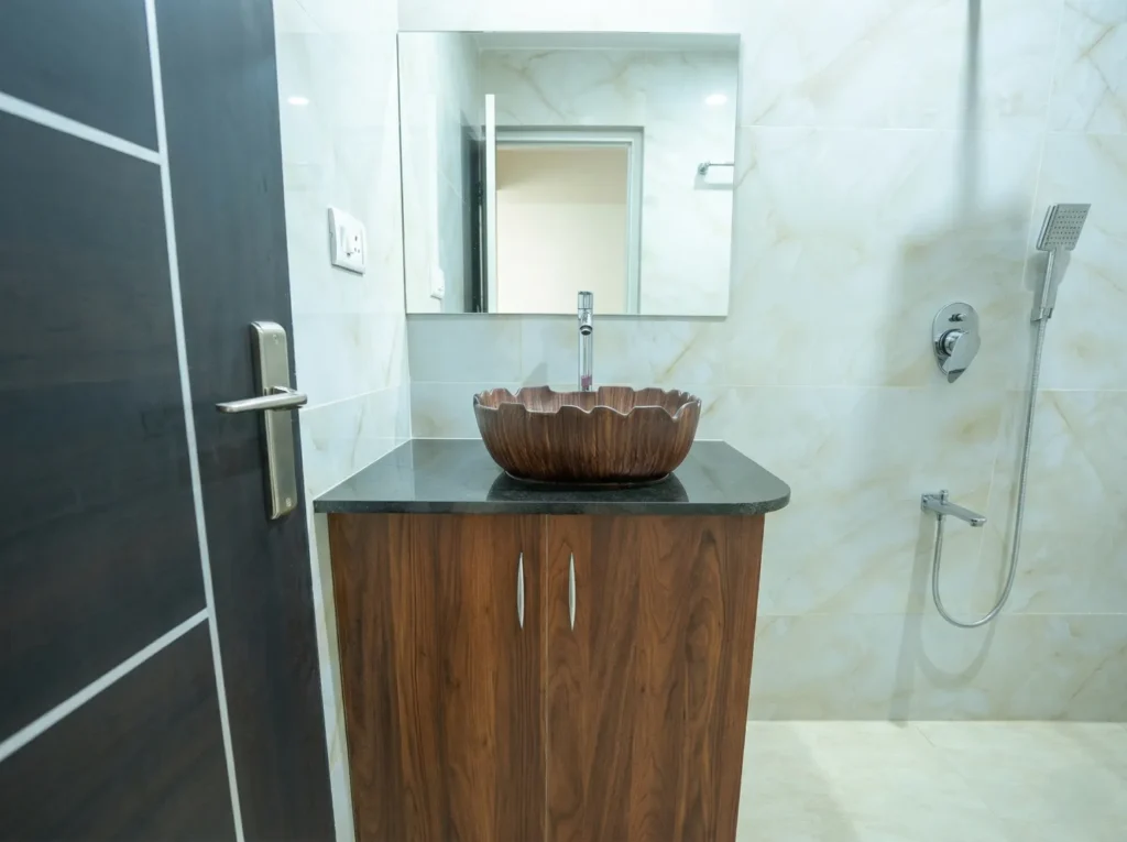 Designer bathroom washbasin area with a unique brown ceramic bowl, black granite counter, and wooden vanity storage.
