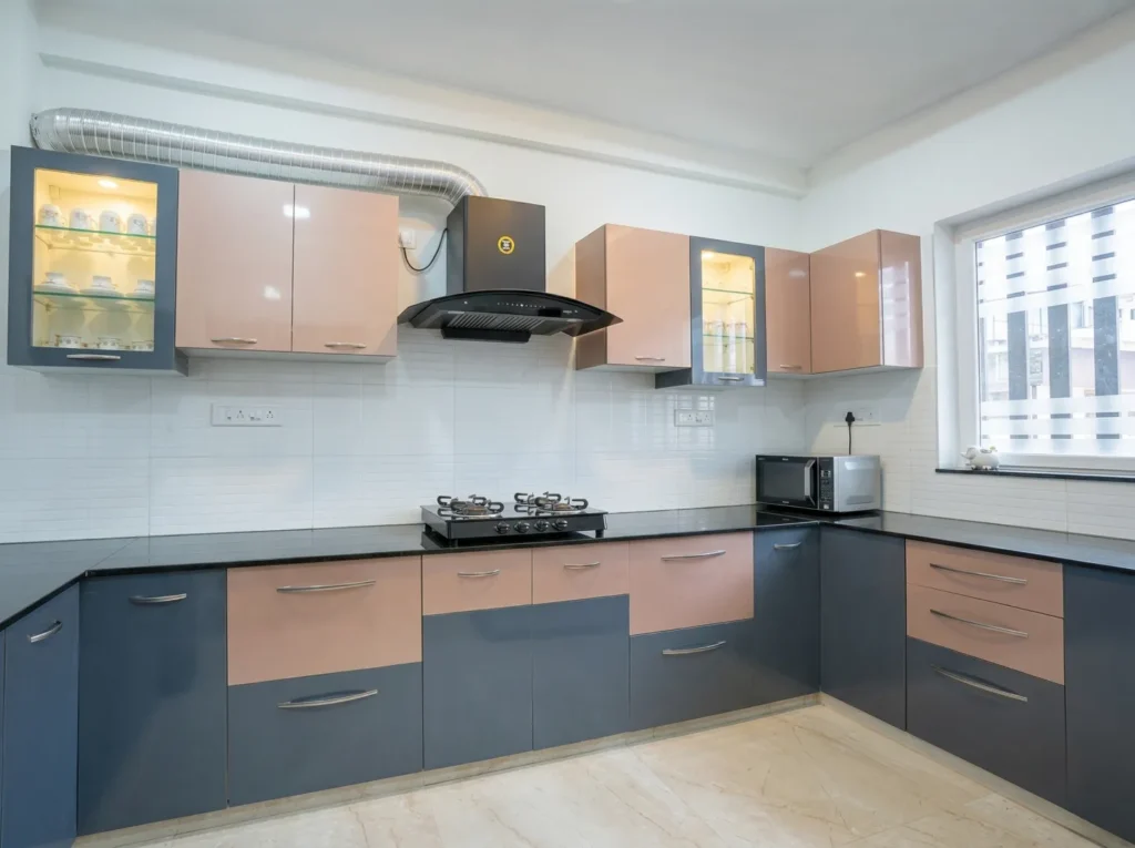 L-shaped modular kitchen with dual-tone peach and blue cabinetry, black granite countertops, and a modern chimney installation.