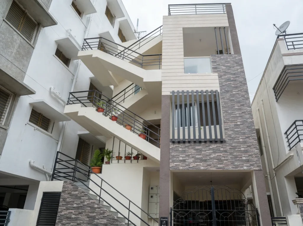 Contemporary residential building elevation with stone-look wall cladding, an external zig-zag staircase, and a modern gated entrance.