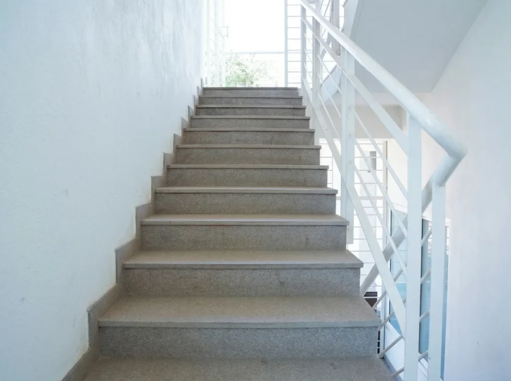 Internal residential staircase design featuring durable polished granite steps and minimalist white safety railings in a turnkey home project.