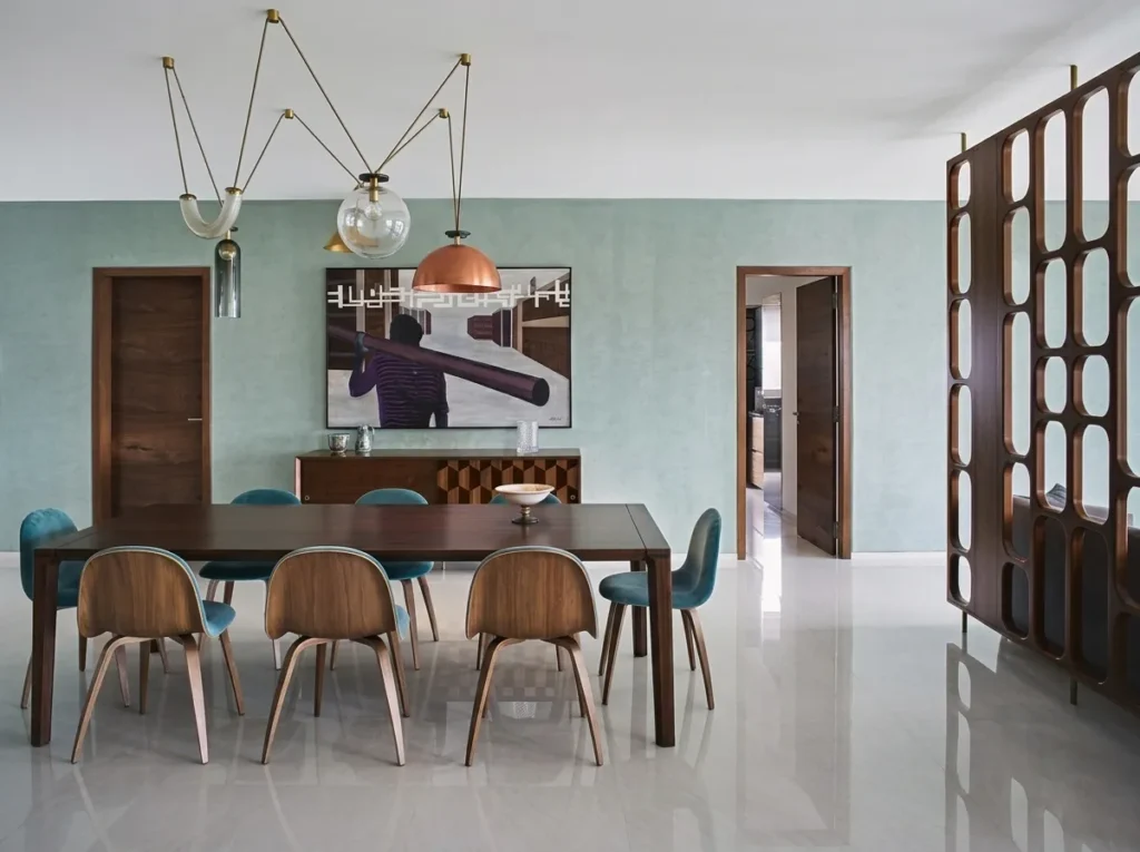 Arun Sky Garden residence – formal dining room with walnut table, teal velvet chairs, multi-pendant brass chandelier, and wooden jaali room divider by High Tech Constructions, Bangalore