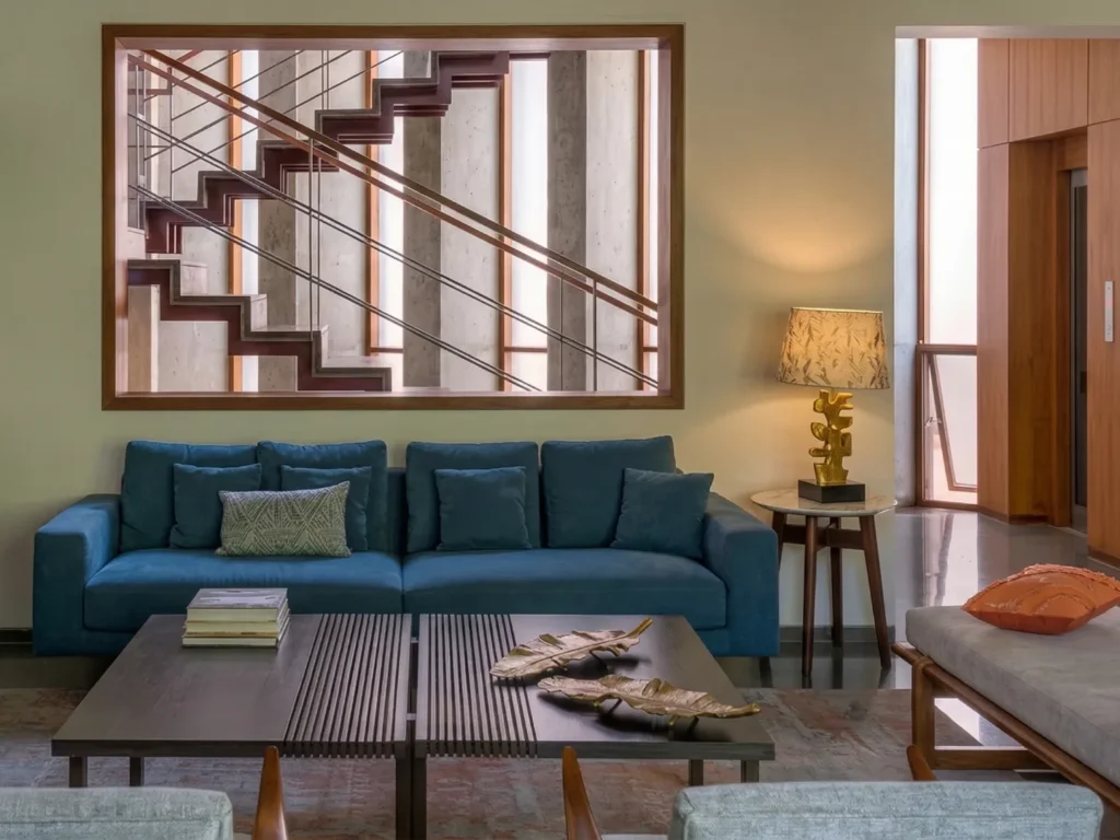 Elegant residential interior construction in Bangalore featuring a framed staircase window view above a teal sofa by High Tech Constructions