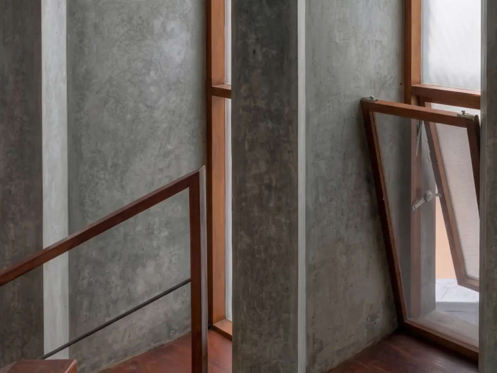 Raw board-formed concrete walls and timber-framed windows at a staircase landing in a Bangalore residential construction project