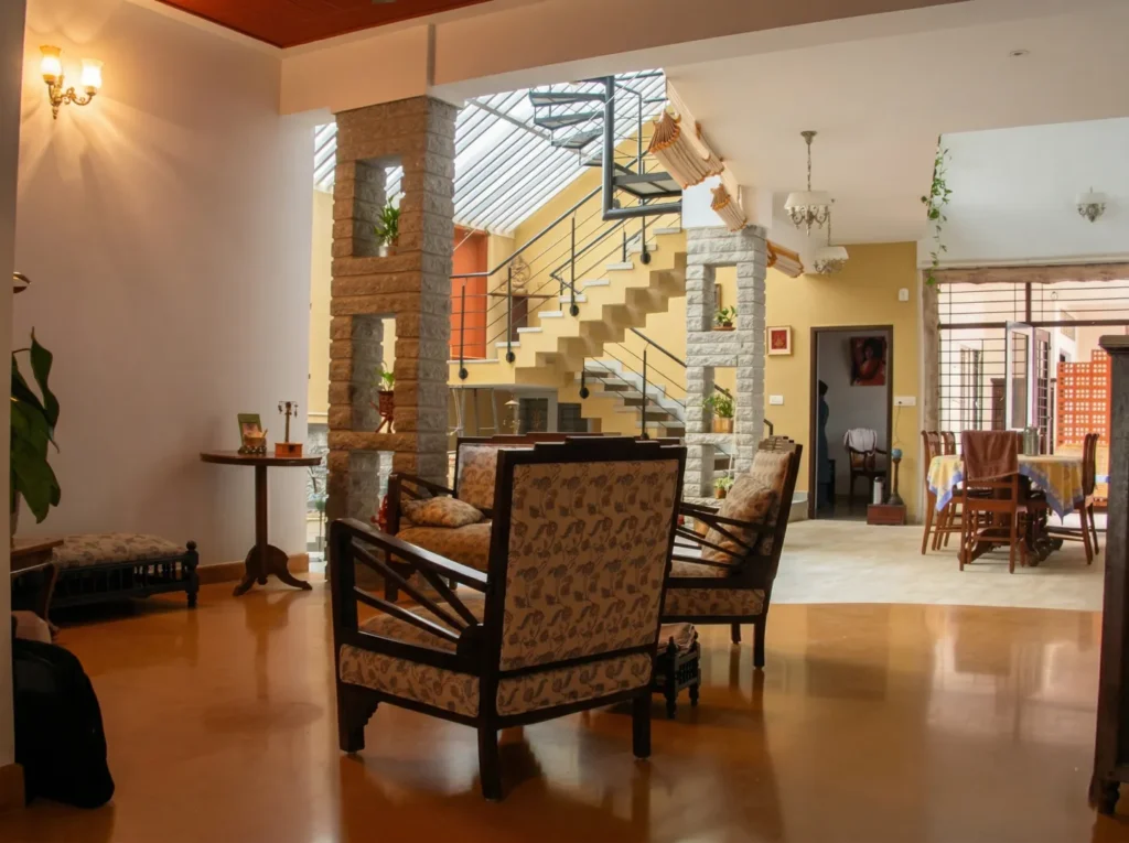 Kalpana turnkey bungalow – open-plan living room with Jaisalmer stone flooring, granite pillars, wooden furniture, and view into central courtyard by High Tech Constructions, Bangalore