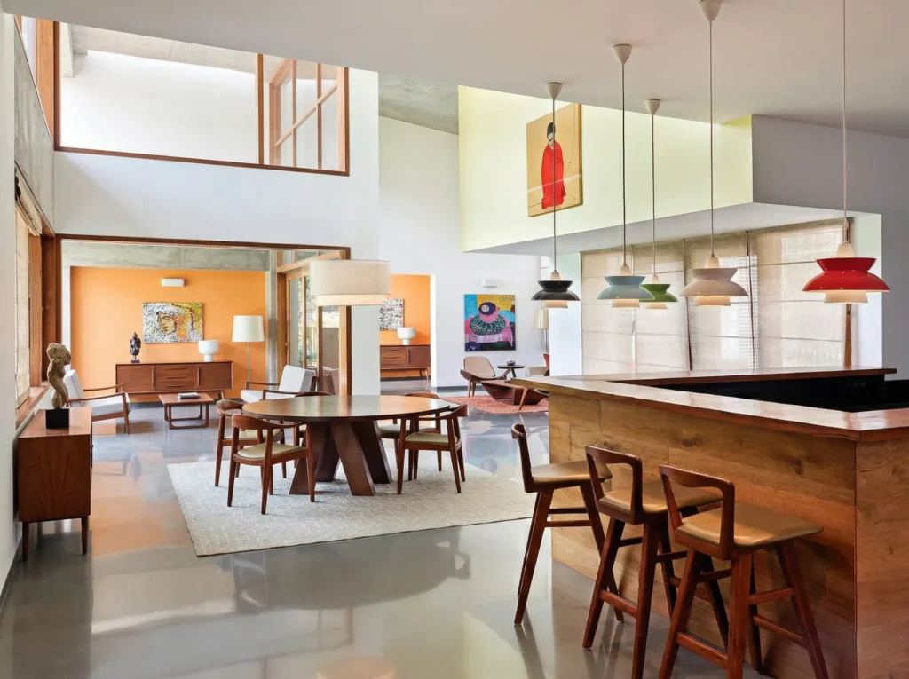 Open-plan residential interior with timber dining set, colourful pendant lights, and kitchen bar in a Bangalore home construction by High Tech Constructions