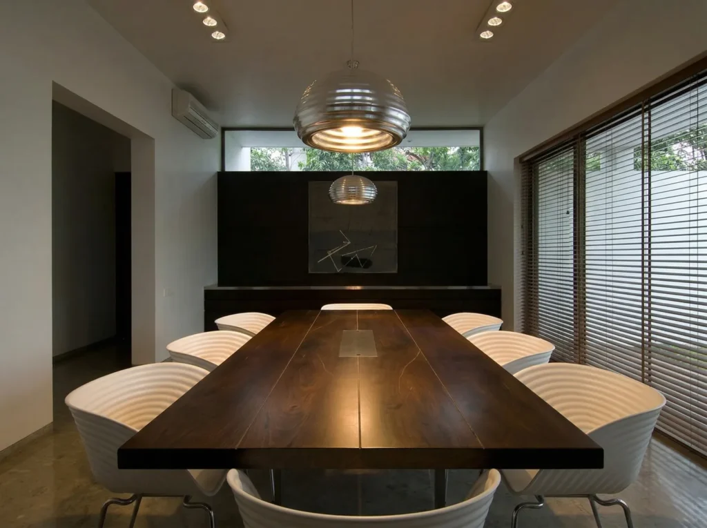 Elegant residential dining room interior construction in Bangalore with dark timber dining table, white sculptural chairs, and chrome globe pendant light
