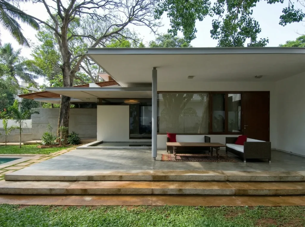 Residential construction in Bangalore with covered outdoor terrace, outdoor lounge seating, swimming pool, and mature tree garden by High Tech Constructions