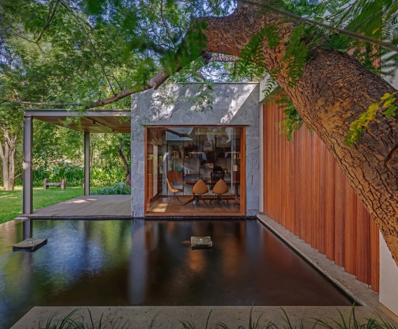 Residential garden study pavilion with granite stone walls, teak-framed glazing, and dark reflecting pool in a Bangalore home construction by High Tech Constructions