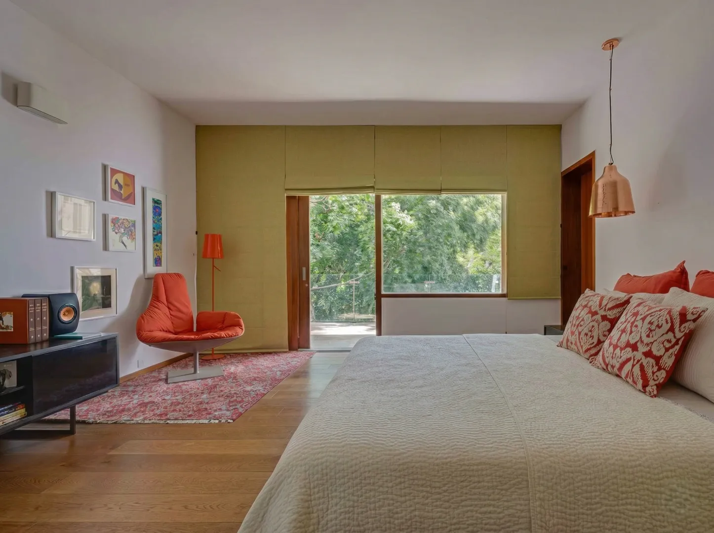 Serene residential master bedroom interior in Bangalore with timber floor, garden view window, orange accent chair, and copper pendant light by High Tech Constructions