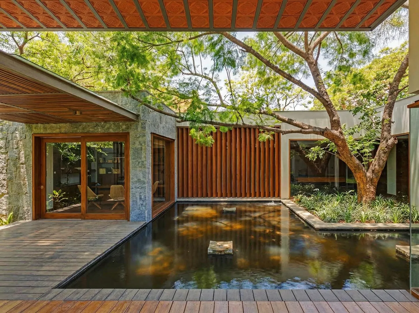Residential courtyard with koi pond, teak louvre screen, granite stone walls, and preserved mature tree in a Bangalore home construction by High Tech Constructions