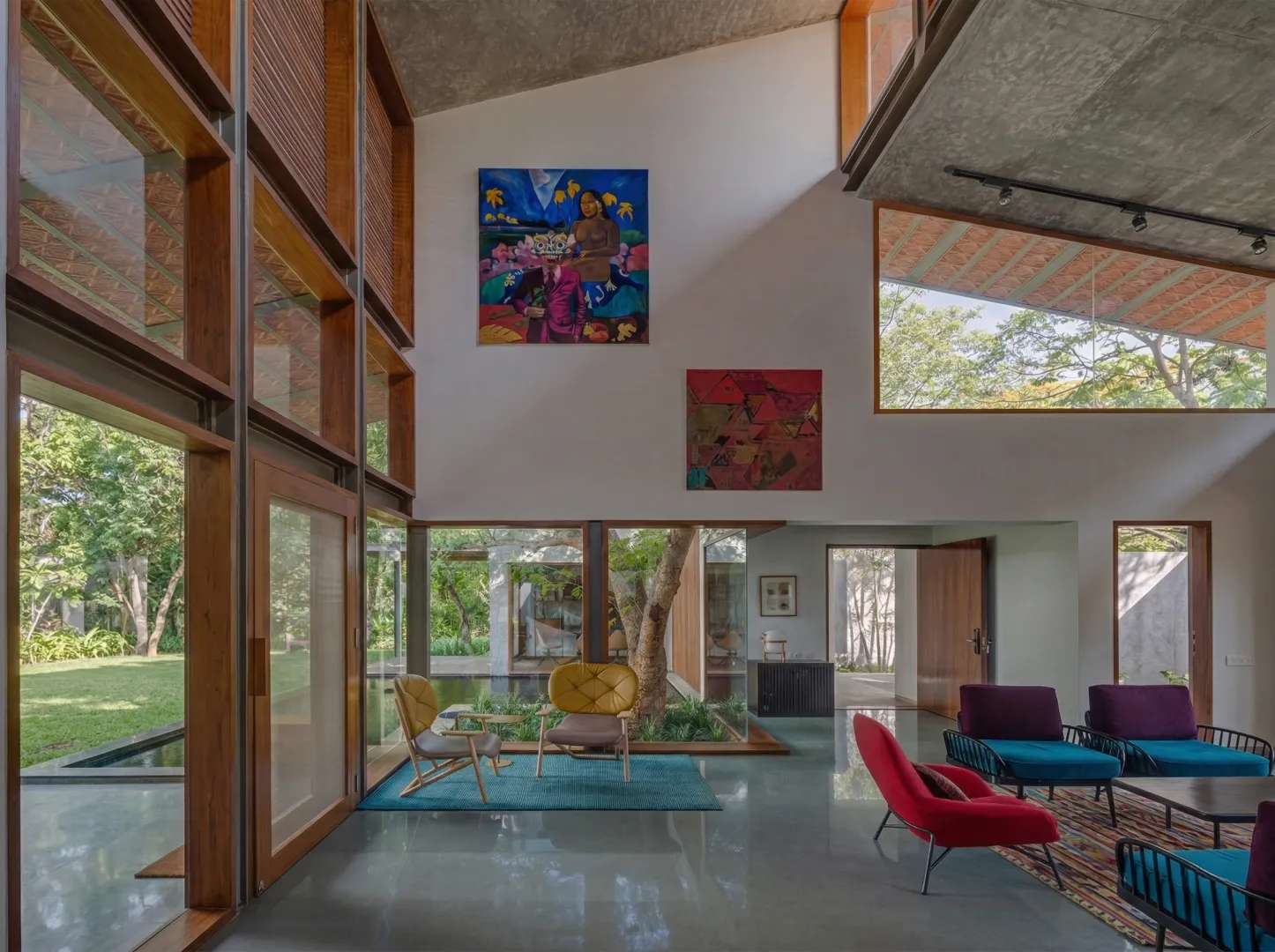 Double-height residential living room interior in Bangalore with large-scale artworks, indoor courtyard tree, and clerestory windows by High Tech Constructions