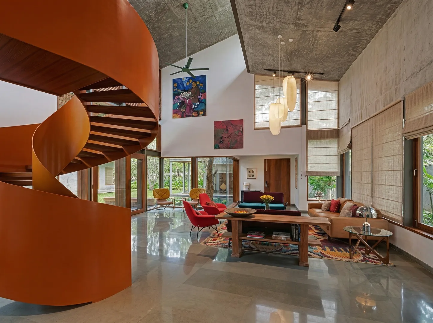 Dramatic residential living room interior in Bangalore with sculptural orange spiral staircase, exposed concrete ceiling, and colourful eclectic furniture by High Tech Constructions