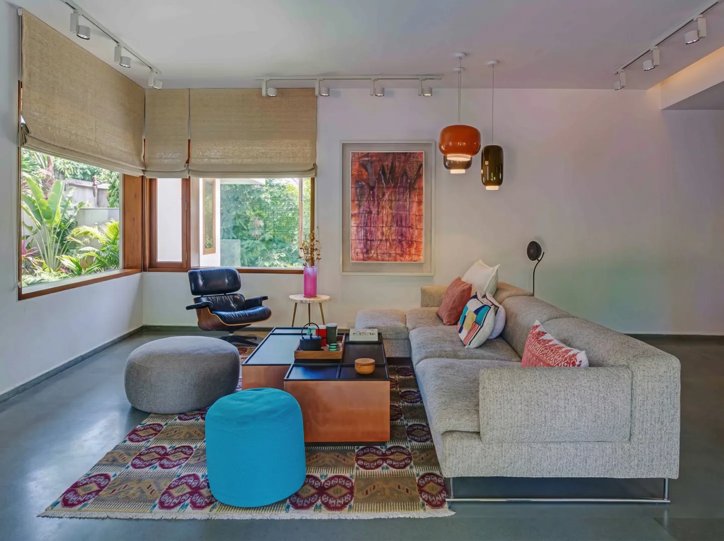 Cosy residential family lounge interior in Bangalore with Eames lounge chair, grey sectional sofa, colourful pendants, and garden view by High Tech Constructions