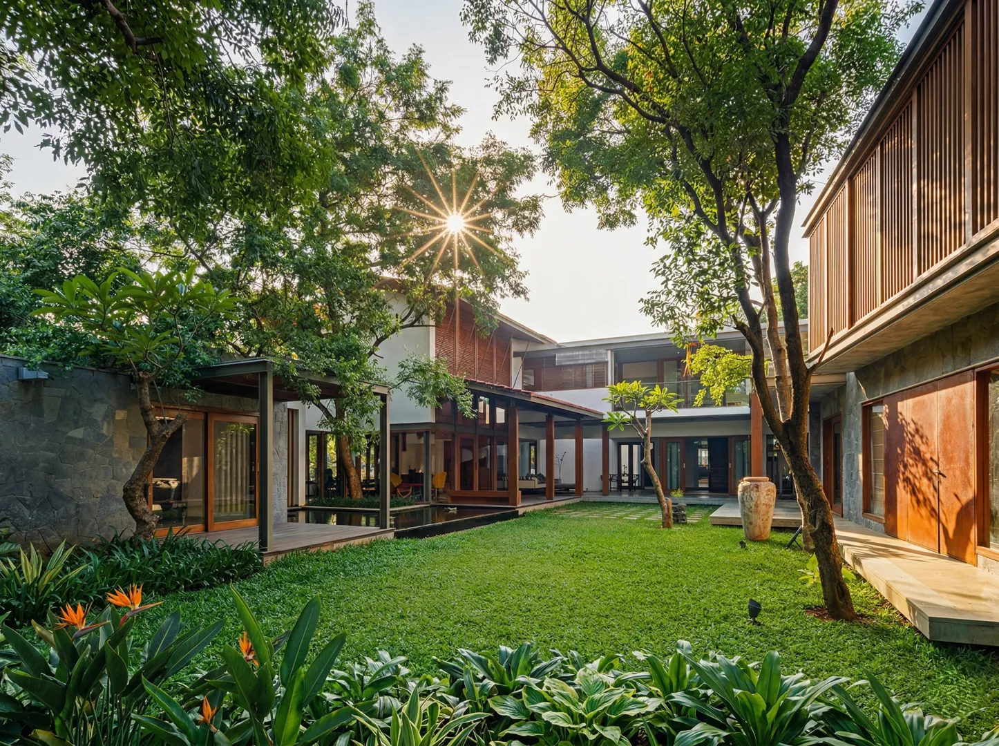 Premium residential home construction in Bangalore with terracotta roof pavilion, teak louvre screen, reflecting pool, and tropical garden at golden hour by High Tech Constructions