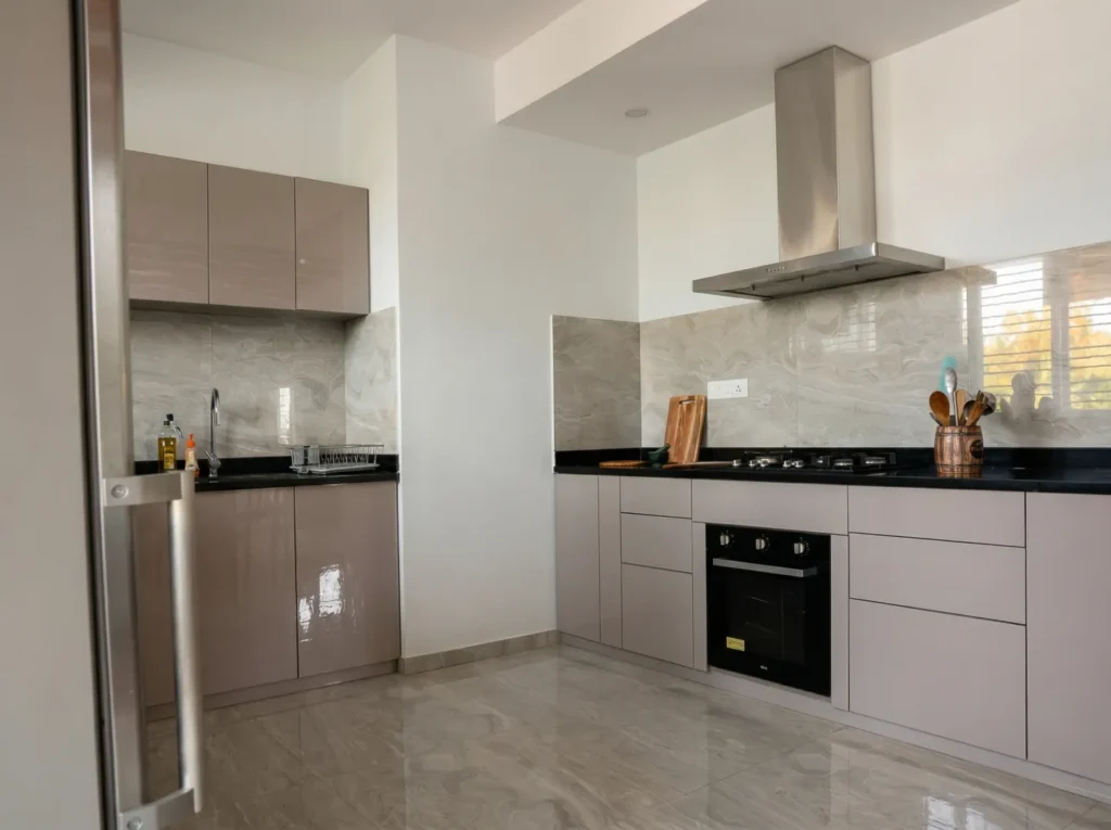 Modern L-shaped modular kitchen with glossy taupe cabinets, black granite countertop, and marble backsplash tiles — home construction Bangalore.
