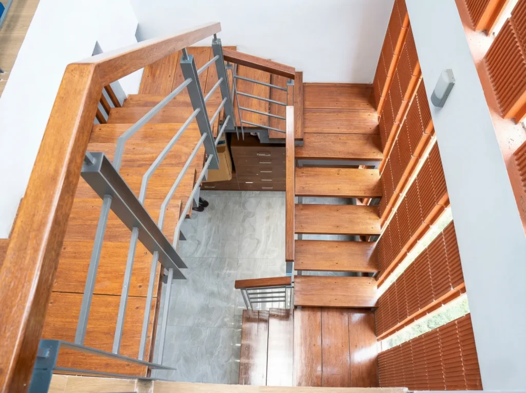 Overhead view of open-riser wooden staircase with steel railings and terracotta brick side screen in a residential home in Bangalore.
