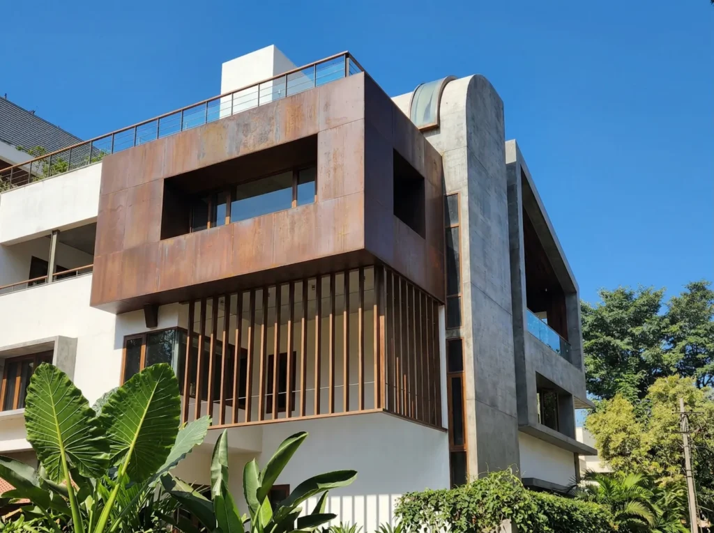 Luxury home exterior with Corten steel cladding, vertical timber louvres, and exposed concrete wall — premium home construction in Bangalore.