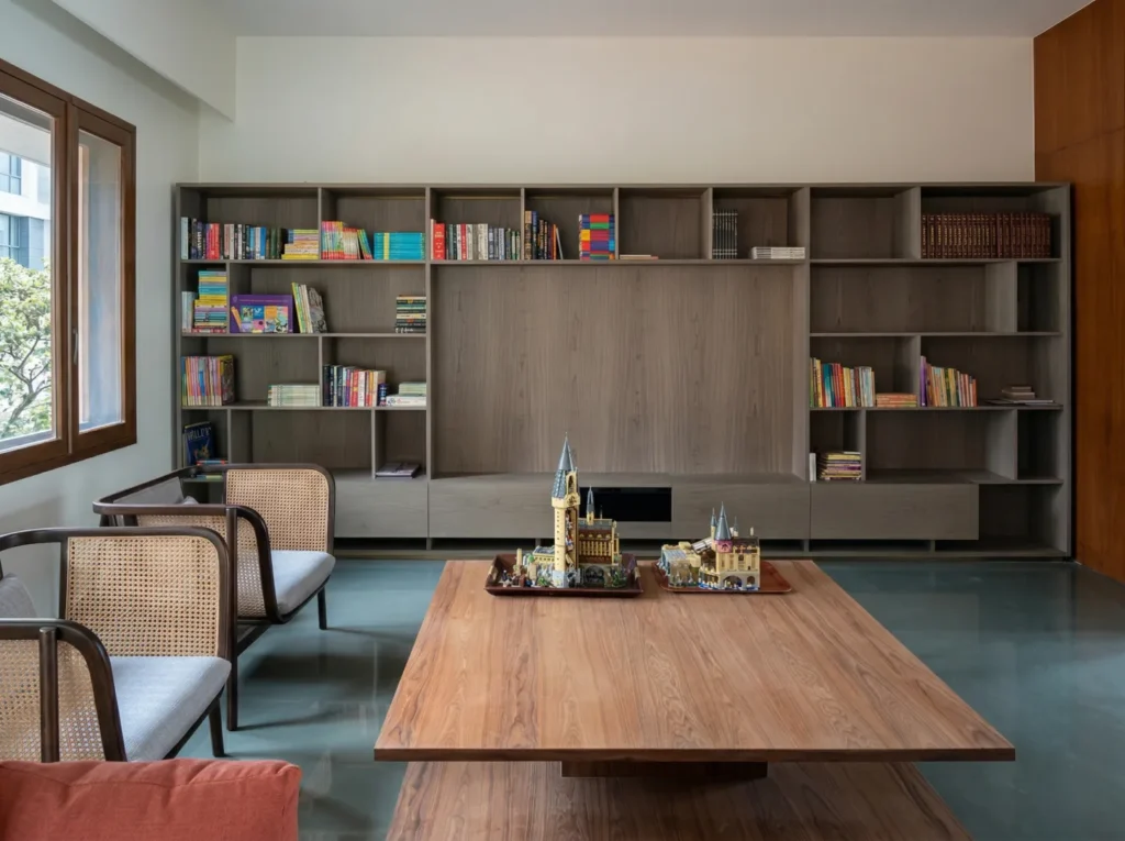 Residential library with full-wall modular walnut shelving, wooden table, and rattan chairs — interiors and construction in Bangalore.