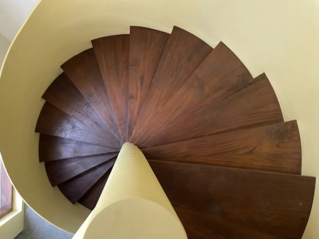 Aerial top-down view of yellow spiral staircase with dark teak timber treads — structure construction detail in a luxury home in Bangalore.