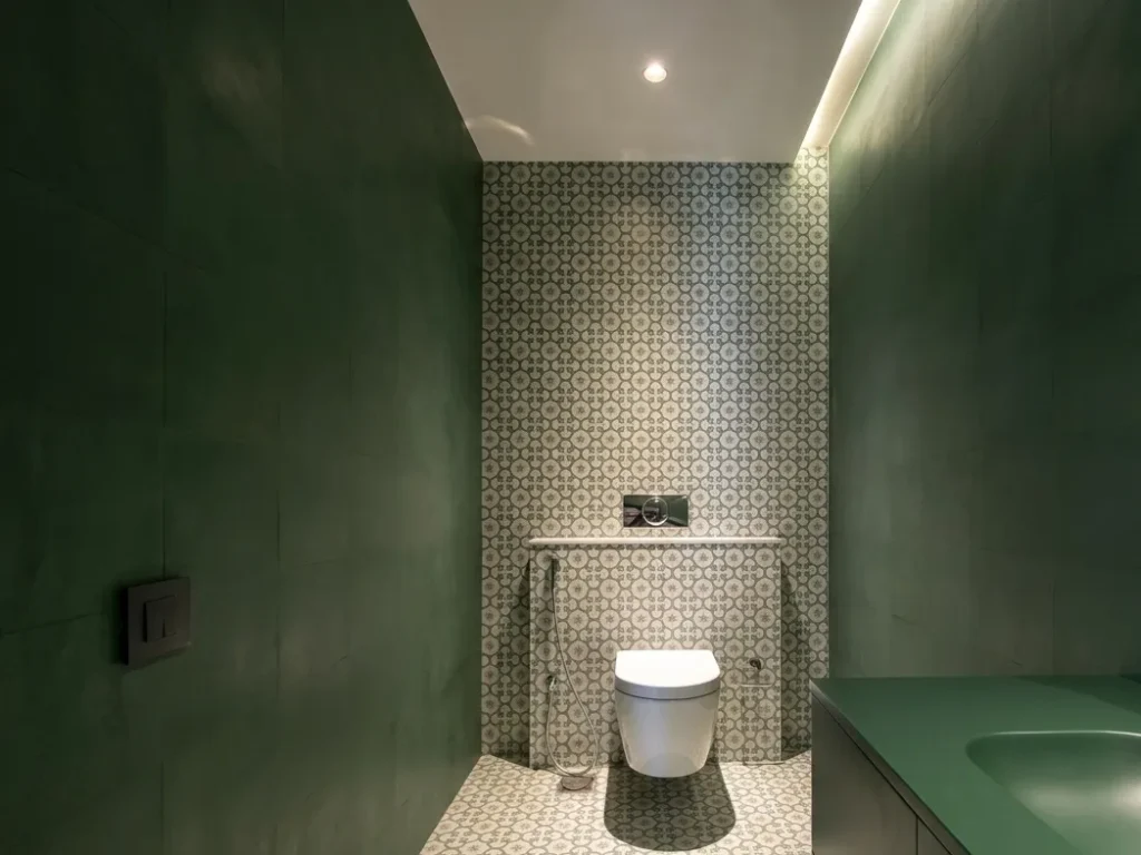 Compact guest toilet with deep forest green walls, patterned encaustic tiles, and wall-hung WC — interior construction detail in Bangalore residence.