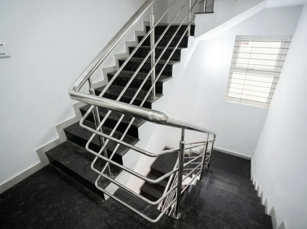 Modern internal staircase featuring black granite steps and high-quality stainless steel (SS) safety railings.