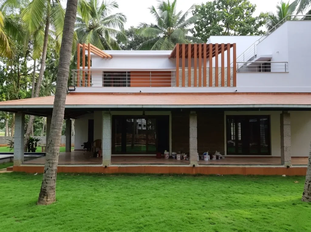 Modern farmhouse architecture featuring a wide terracotta-tiled porch, granite pillars, and a contemporary second-floor terrace with wooden pergola accents.