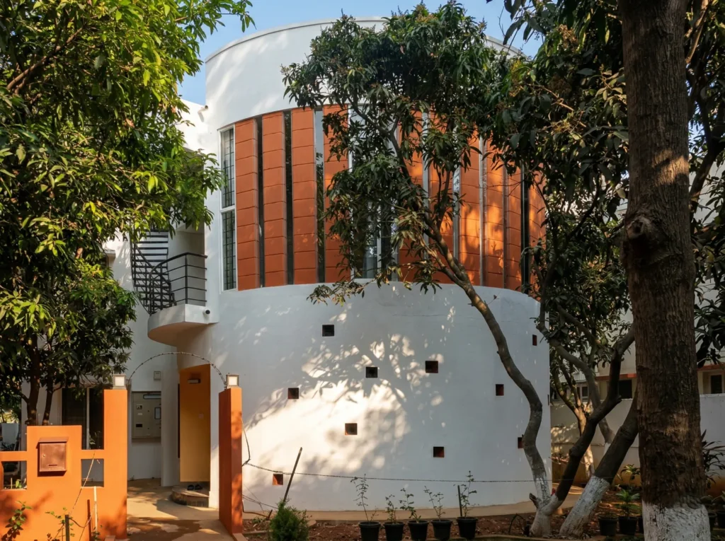 Unique circular residential architecture featuring a white curved facade, vertical terracotta brick slits, and integrated spiral staircase.