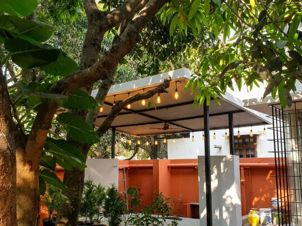 Modern outdoor pavilion design with a white cantilevered roof, decorative Edison bulb string lights, and lush garden surroundings.