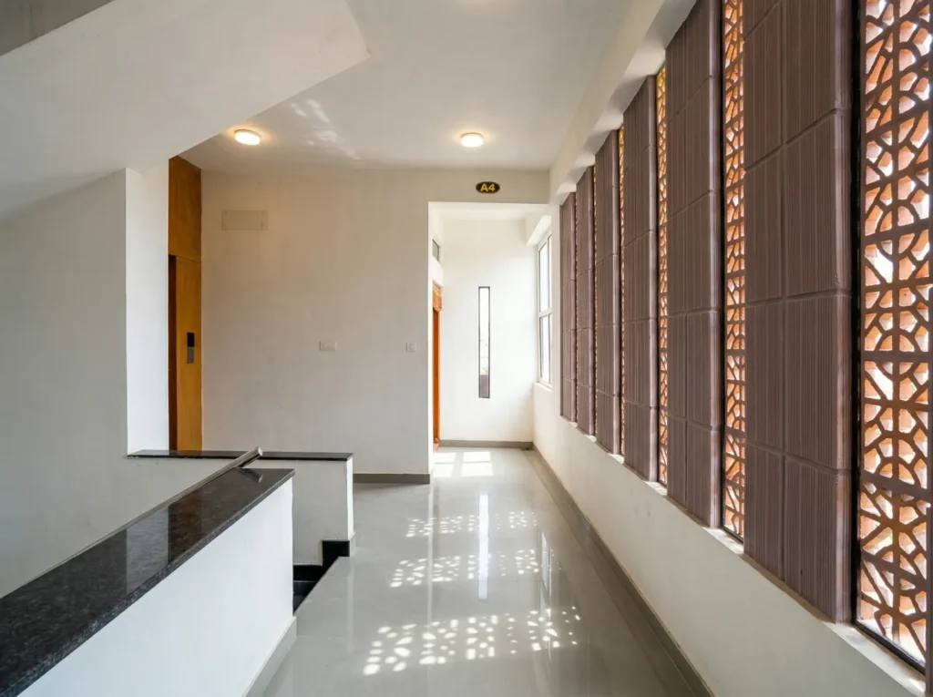 Bright apartment corridor with terracotta jali screen by a home construction company in Bangalore.