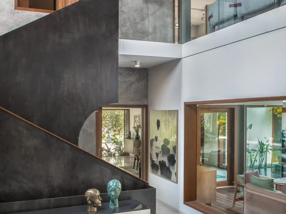 Residential staircase hall in Bangalore with dark steel stair cladding, original artworks, bronze sculptures, and teak-framed koi pond view by High Tech Constructions
