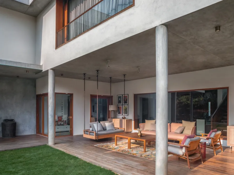 Residential covered outdoor living terrace with hanging timber swing sofa, rattan seating, teak deck, and garden lawn in a Bangalore home construction by High Tech Constructions