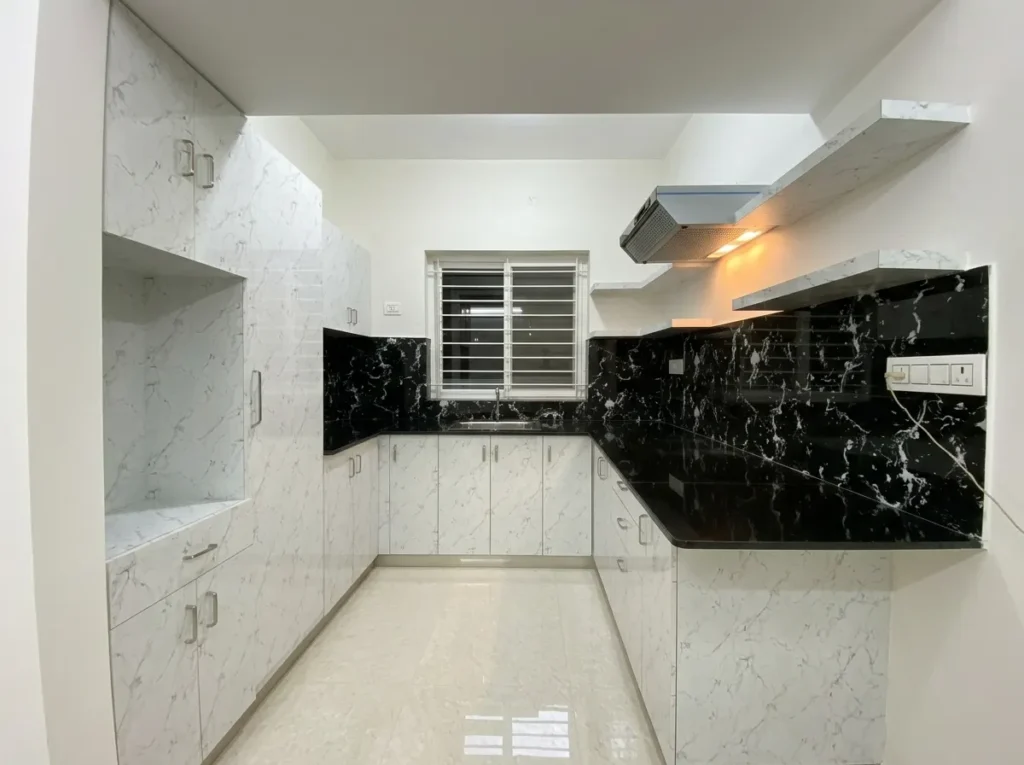 Modern U-shaped modular kitchen design featuring white marble-finish cabinetry, black granite countertops, and integrated chimney hood.