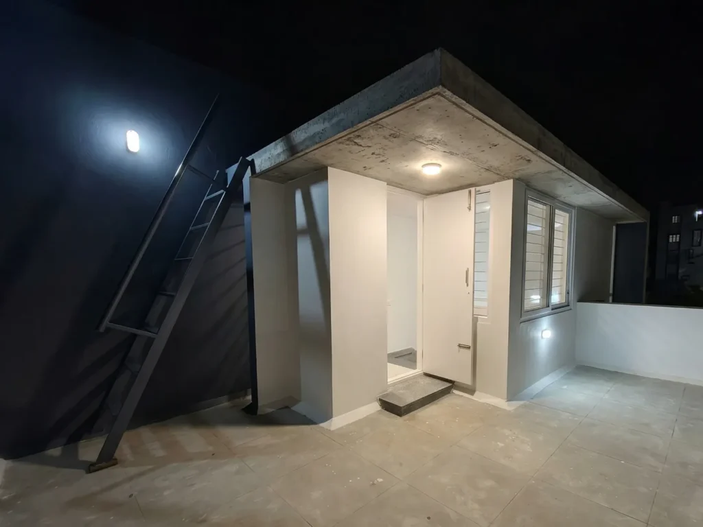 Contemporary rooftop terrace design with an exposed concrete canopy, industrial-style metal ladder, and weather-proof outdoor lighting.