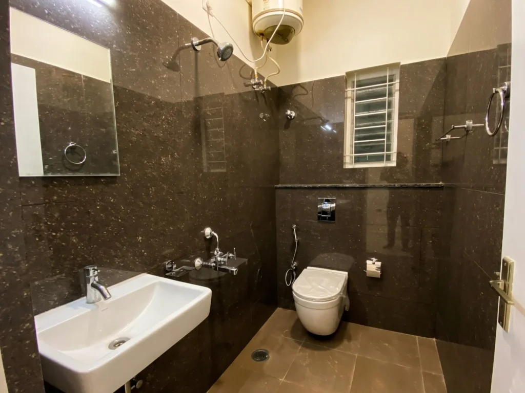 Luxury bathroom interior with dark brown marble-patterned wall tiles, wall-mounted commode, and high-quality chrome bathroom fittings.