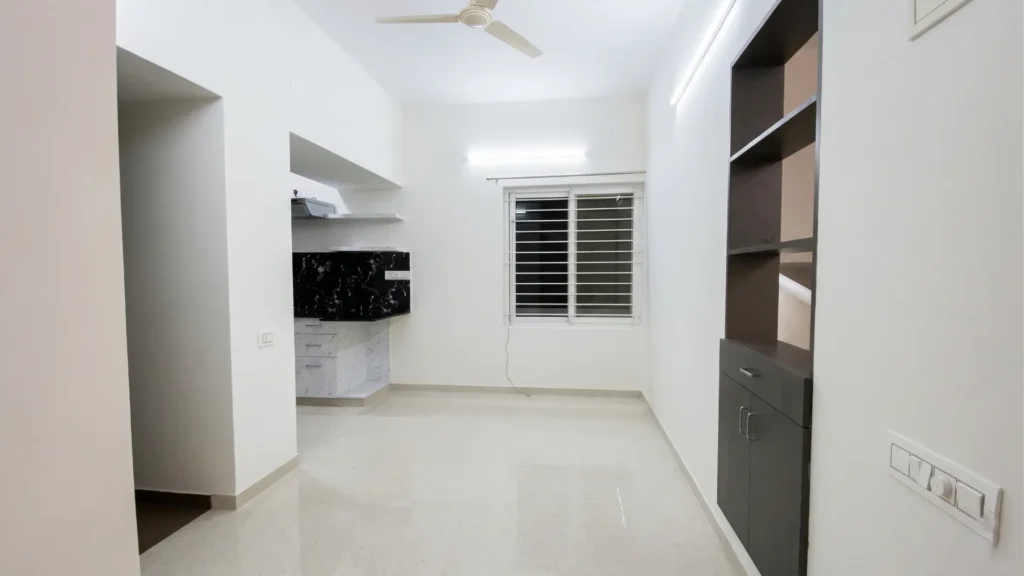 Minimalist living room interior featuring polished vitrified flooring, built-in dark wood shelving, and natural light from large windows.