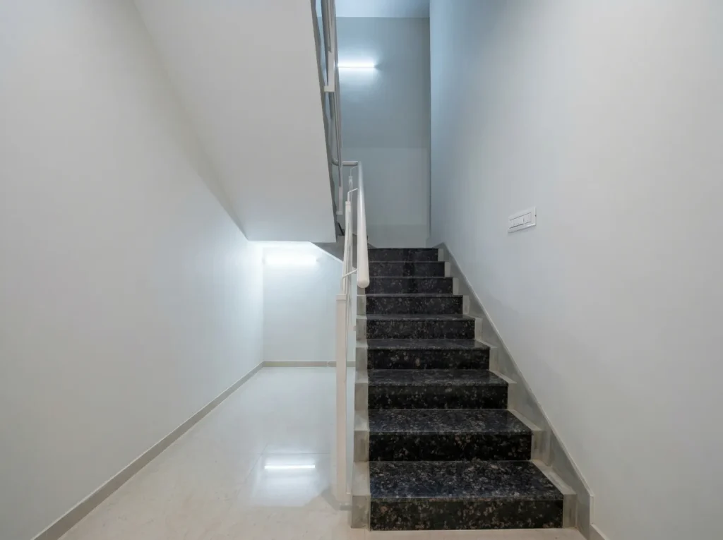 Modern internal staircase design with dark granite steps, white safety railings, and integrated wall-recessed LED lighting.