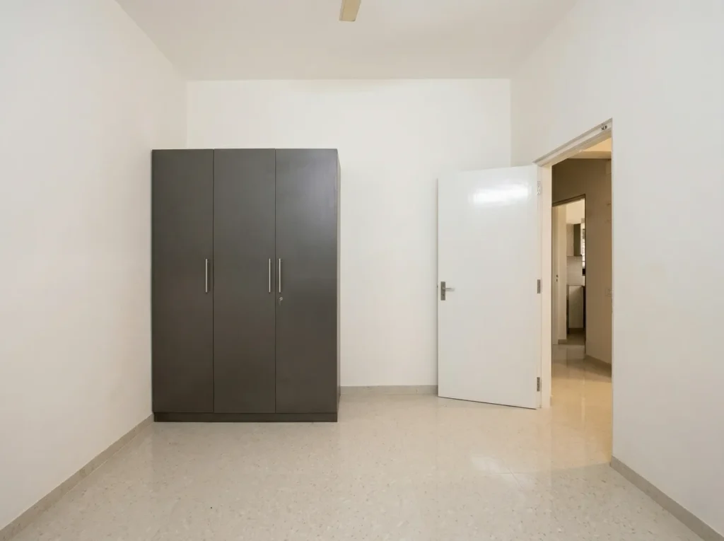 Modern bedroom interior showing a three-door matte grey wardrobe, premium vitrified tiles, and a clean white minimalist paint finish