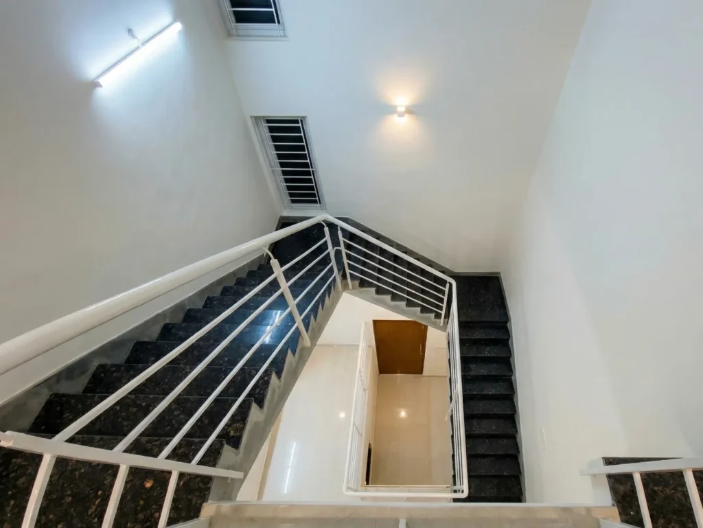 Bird's eye view of a luxury duplex staircase with dark granite treads, white powder-coated railings, and a multi-level open foyer.