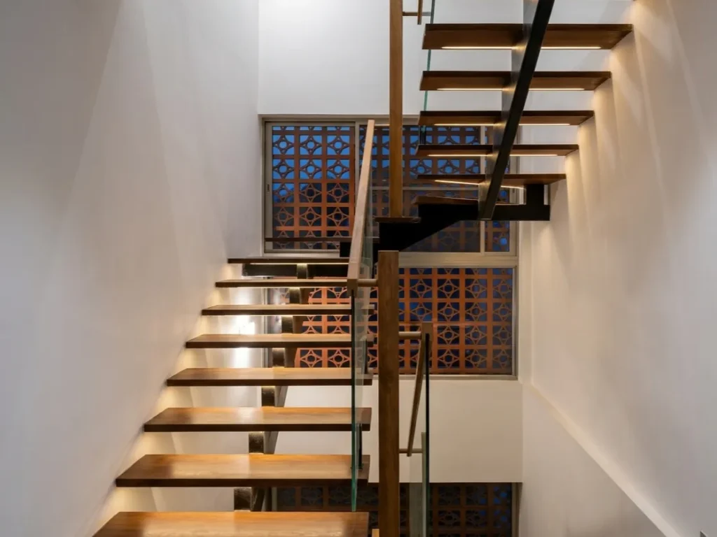 Floating timber staircase with glass balustrade and decorative jaali screen window in a Bangalore residential interior construction by High Tech Constructions