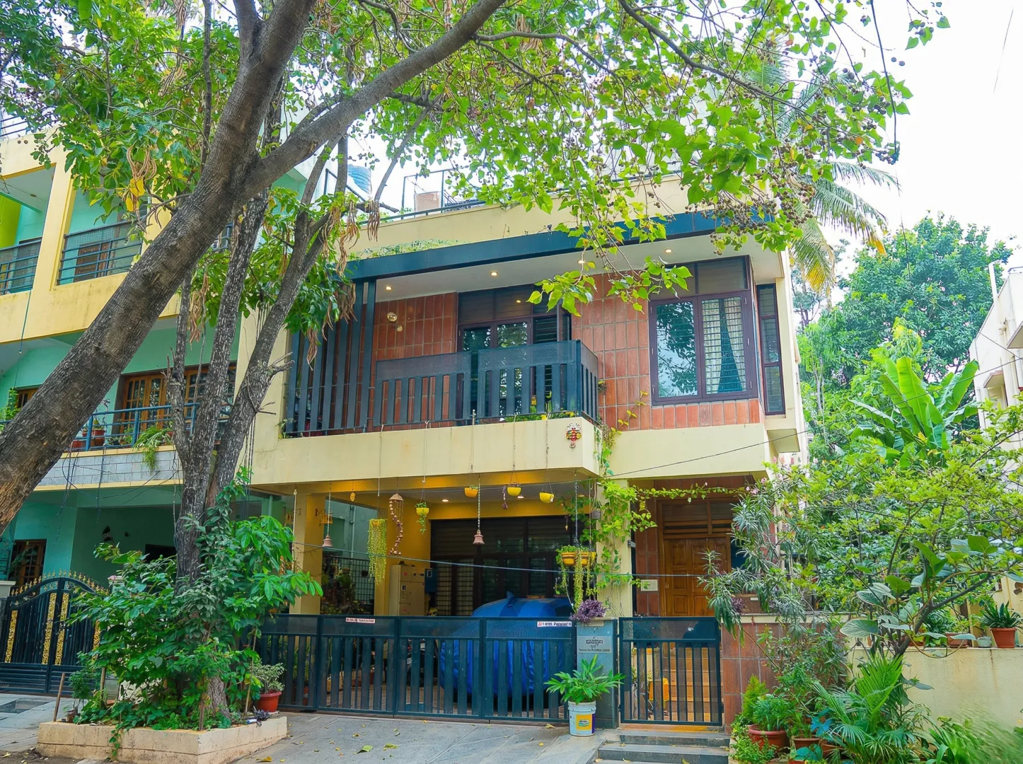 Anand Prakash residence – front elevation with clay tile cladding, MS balcony railing, verandah seating, and lush garden landscaping by High Tech Constructions, Bangalore