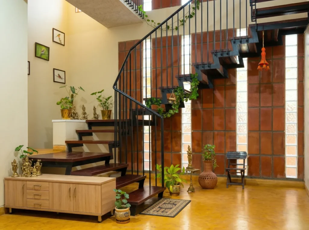 Anand Prakash residence – interior spiral staircase with MS railing, clay brick and glass block wall, red oxide flooring, and traditional brass decor by High Tech Constructions, Bangalore