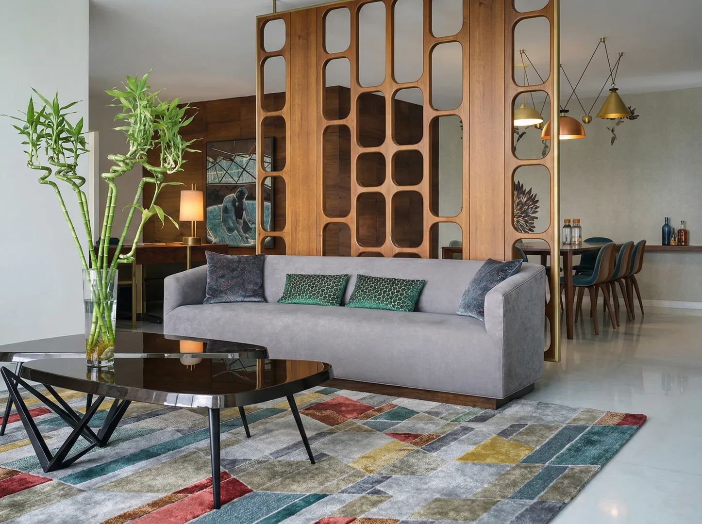 Arun Sky Garden residence – open-plan living area with grey velvet sofa, geometric coffee table, multicolour rug, and carved wooden room divider separating dining space by High Tech Constructions, Bangalore