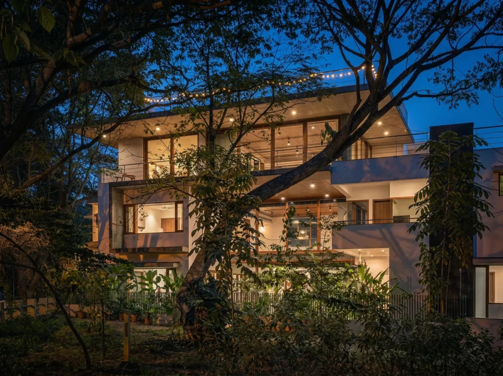 Illuminated multi-storey residential home construction in Bangalore glowing warmly at dusk, set among mature trees