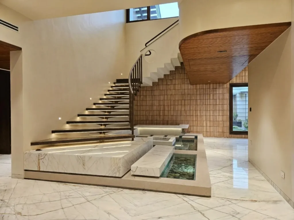 Luxury residential interior with floating marble staircase, water feature, and timber ceiling in a Bangalore home construction by High Tech Constructions
