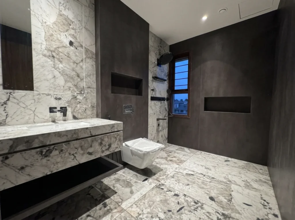High-end residential bathroom with full marble cladding, dark micro-cement walls, and walk-in shower in a Bangalore home construction project