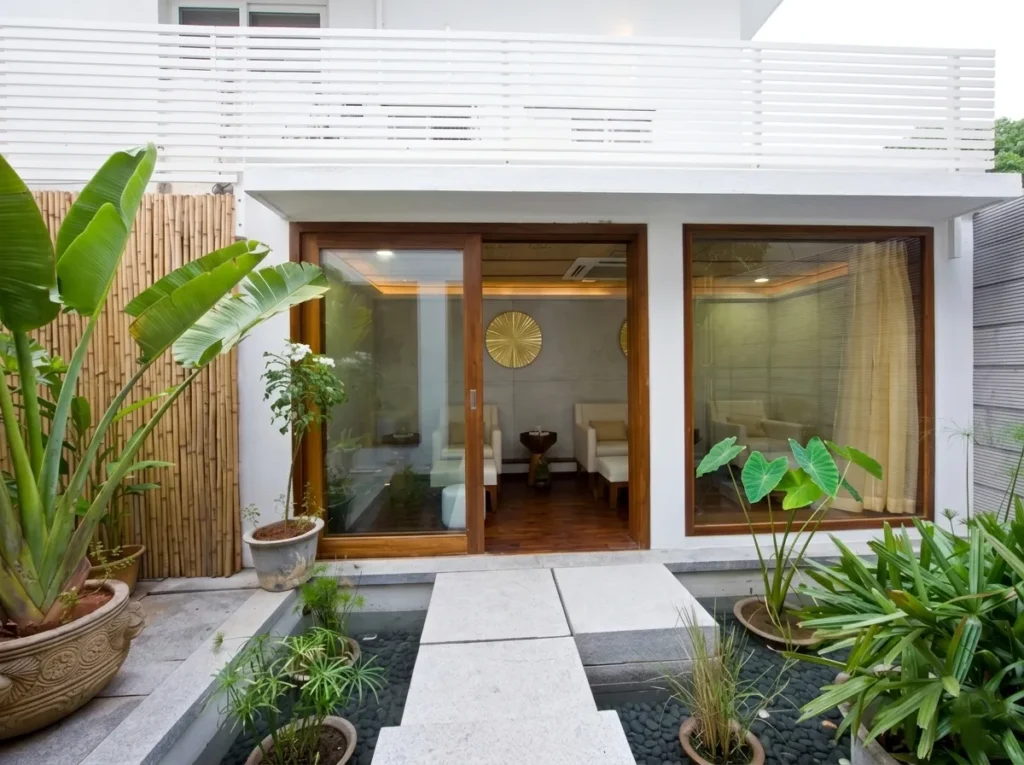 Commercial spa exterior entrance in Bangalore with tropical garden planting, bamboo screen, teak-framed glazing, and stone path by High Tech Constructions