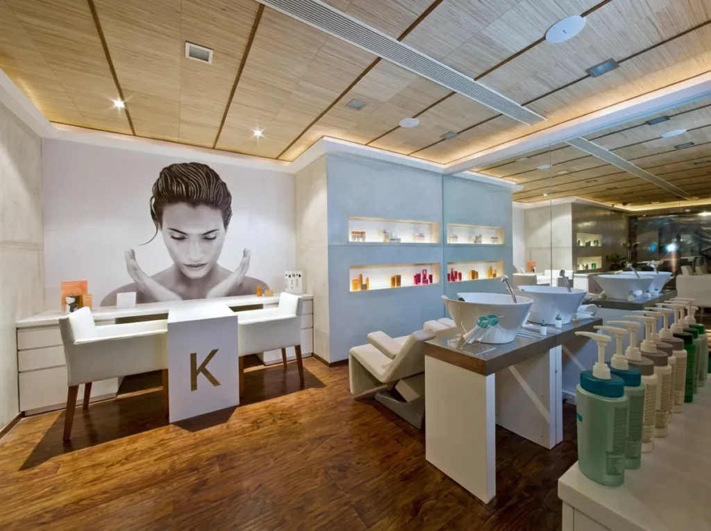 Commercial salon interior construction in Bangalore with timber ceiling, illuminated product niches, shampoo stations, and large-format brand mural by High Tech Constructions